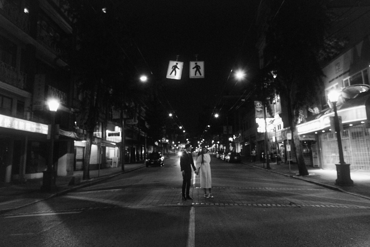 bride and groom holding hands while standing in the middle of the street in vancouver chinatown