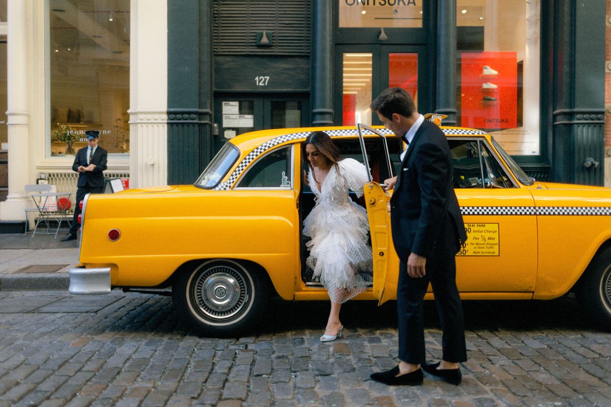 editorial style wedding photo of groom helping bride out of a classic NYC checkered cab