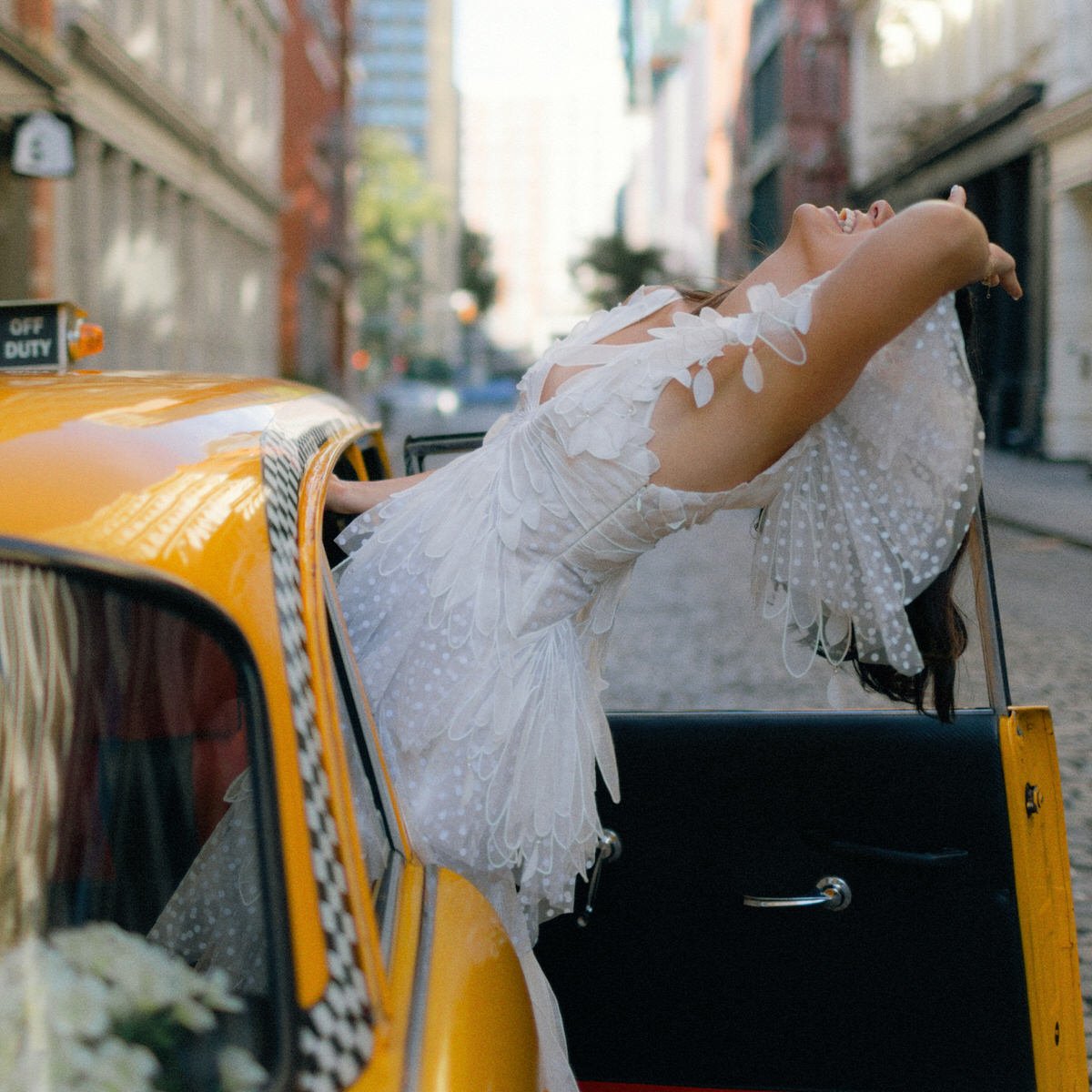 bride posing playfully with a New York checkered cab in Manhattan
