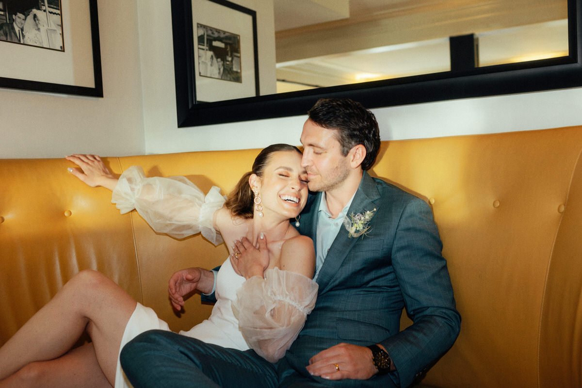 bride and groom happily posing in front of yellow seating at Teahouse Stanley Park