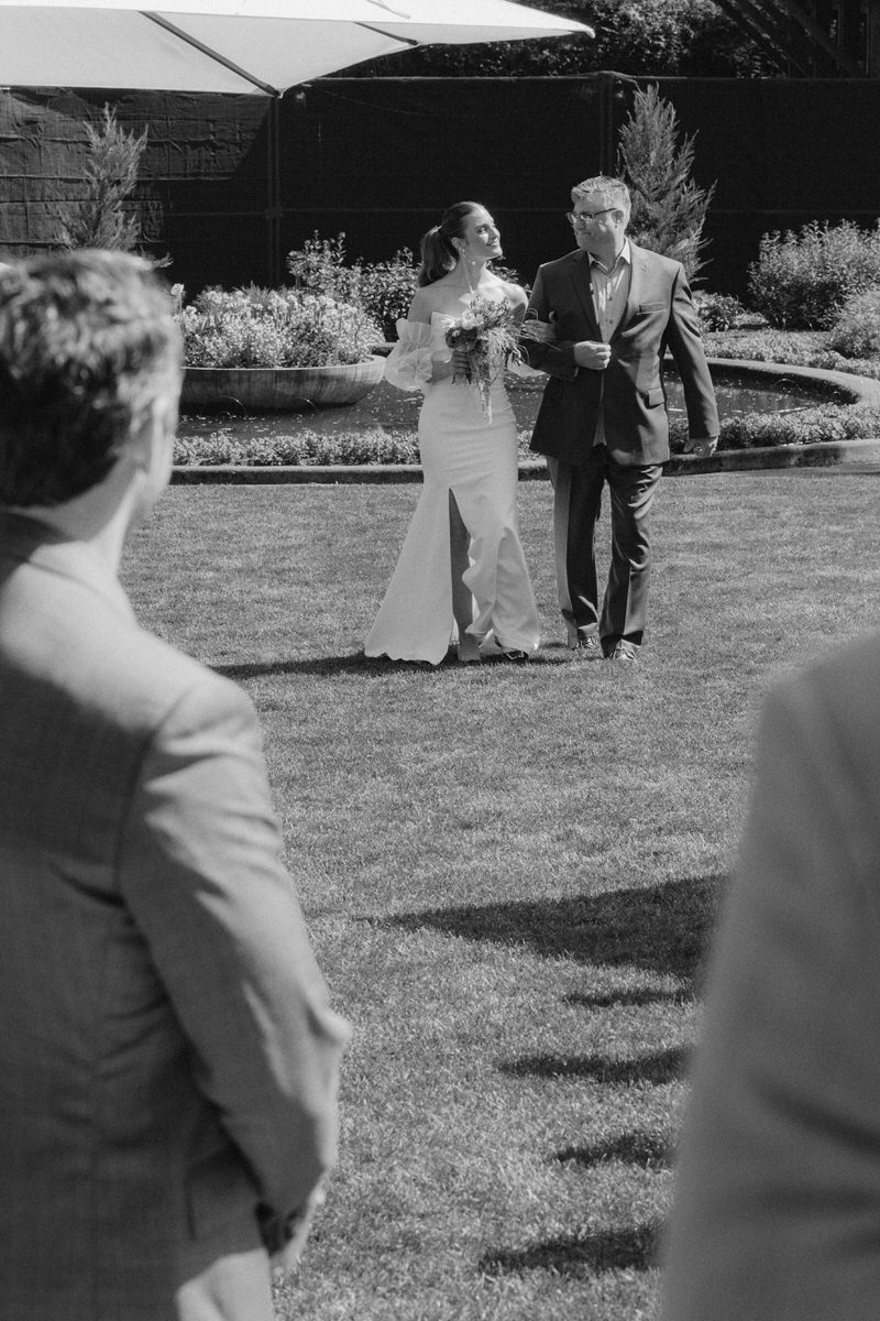 bride smiling towards her father while walking into the ceremony together in Vancouver