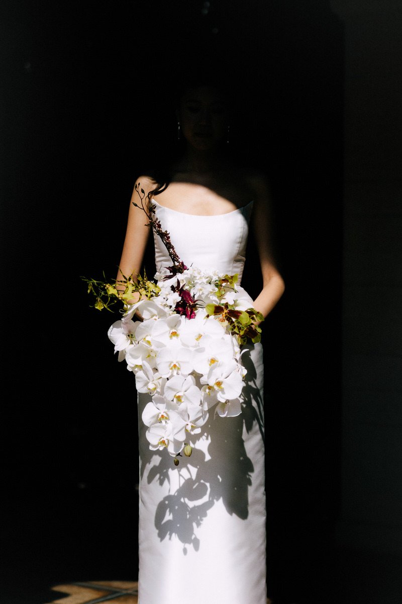 bride holding a large orchid bouquet while obscured by shadow
