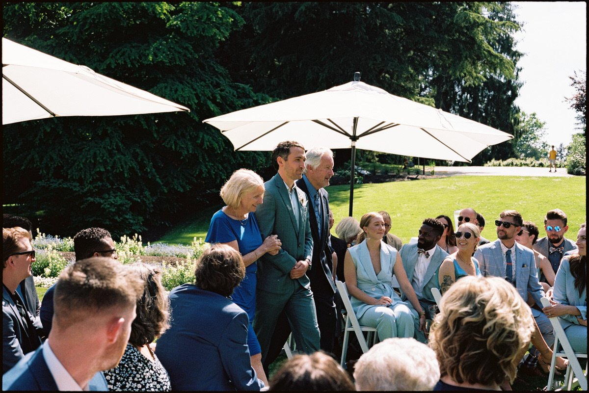 35mm film photo of groom walking into ceremony with his parents in Stanley Park