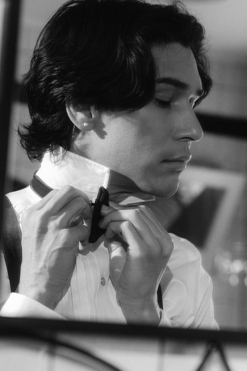handsome groom wearing pearl earring and tying his bow tie