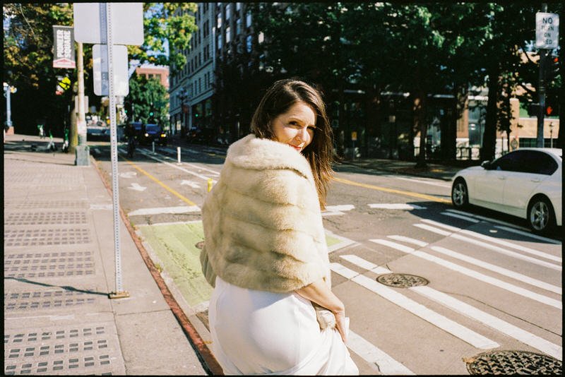 35mm film photo of bride wearing a fur shawl. she is crossing the street in downtown Seattle