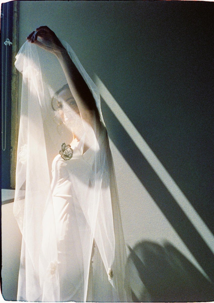 35mm film photo of bride holding her veil as natural light streams through a window in Philadelphia