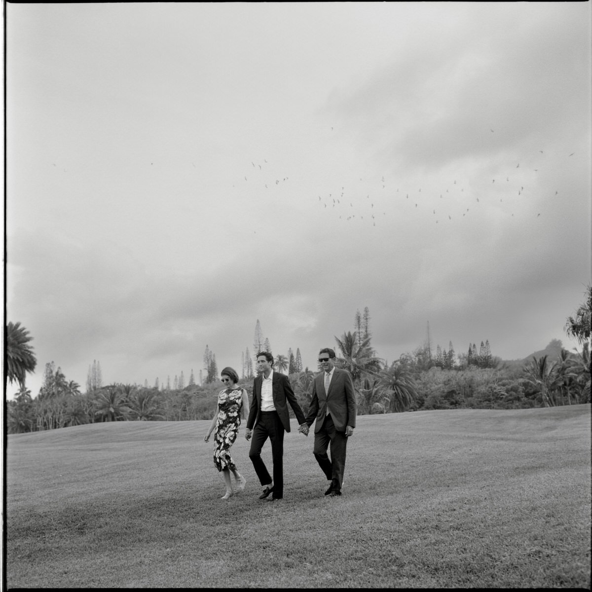 medium format photo of groom and parents entering wedding ceremony as birds fly overhead against a stormy sky