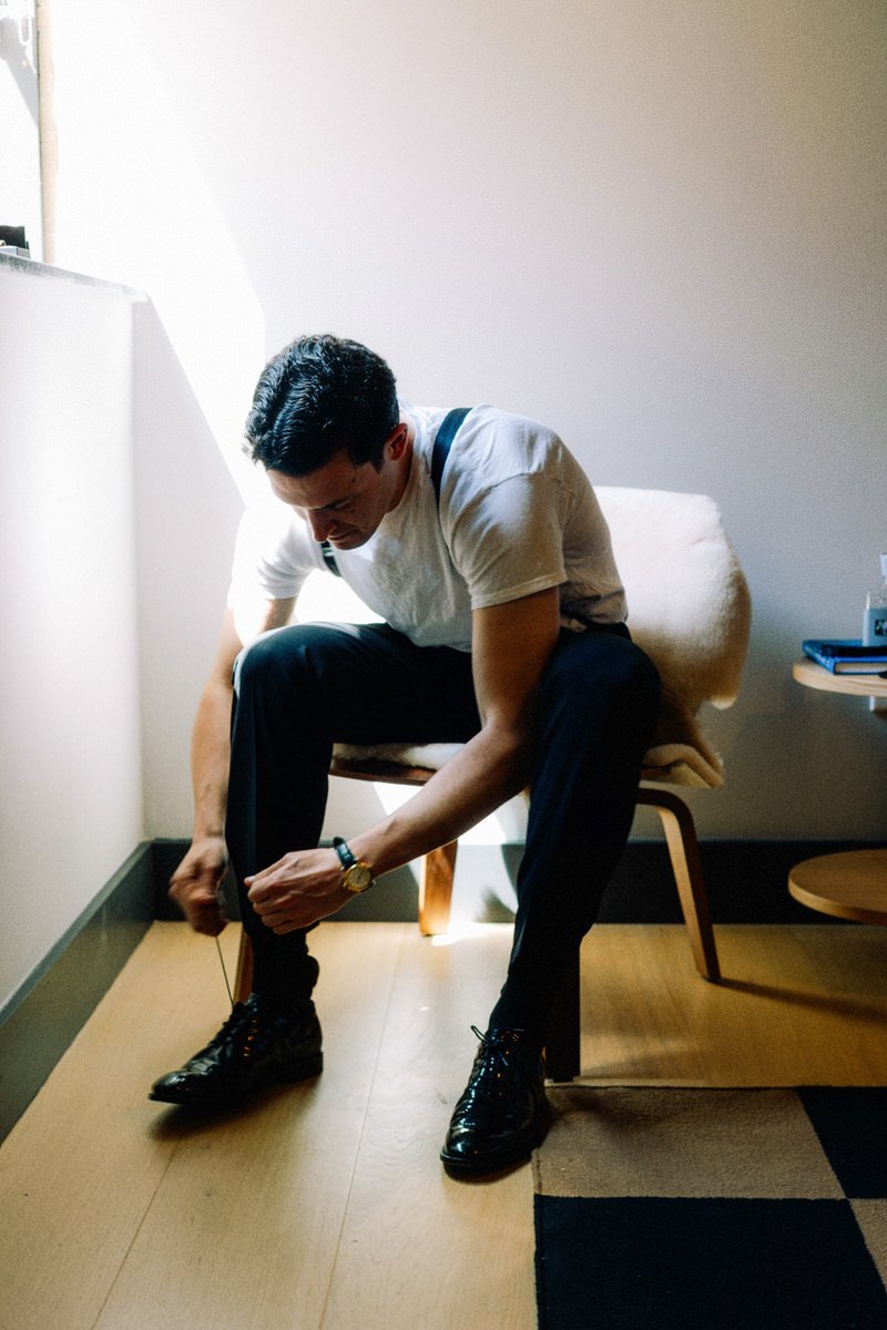groom tying his shoes inside his hotel room at the Switch House by Cescaphe