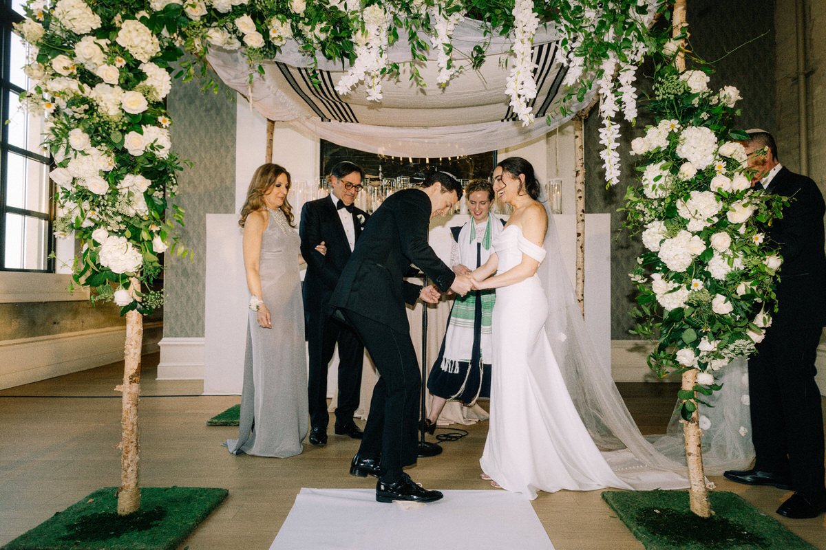 groom breaking the glass during a Jewish wedding at the Switch House by Cescaphe. the green and white Chuppah frames the scene perfectly