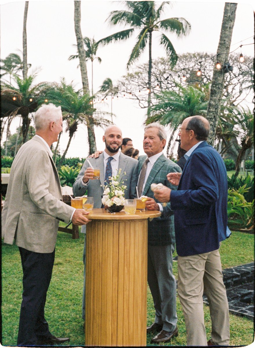 35mm film photo of wedding guests standing around a wooden round bar table during cocktail hour in Maui