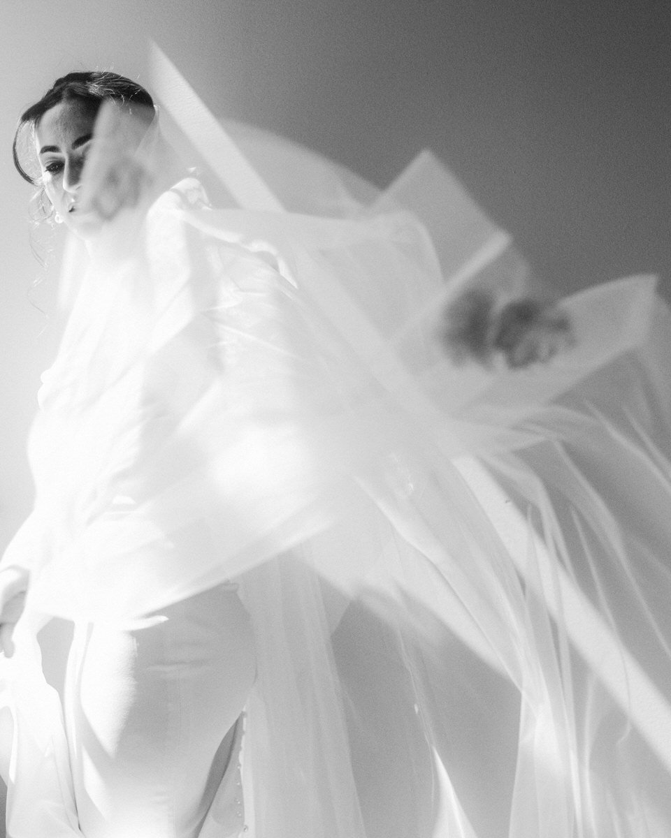 bride ruffling her veil while illuminated by natural window light in her hotel room at the Switch House by Cescaphe