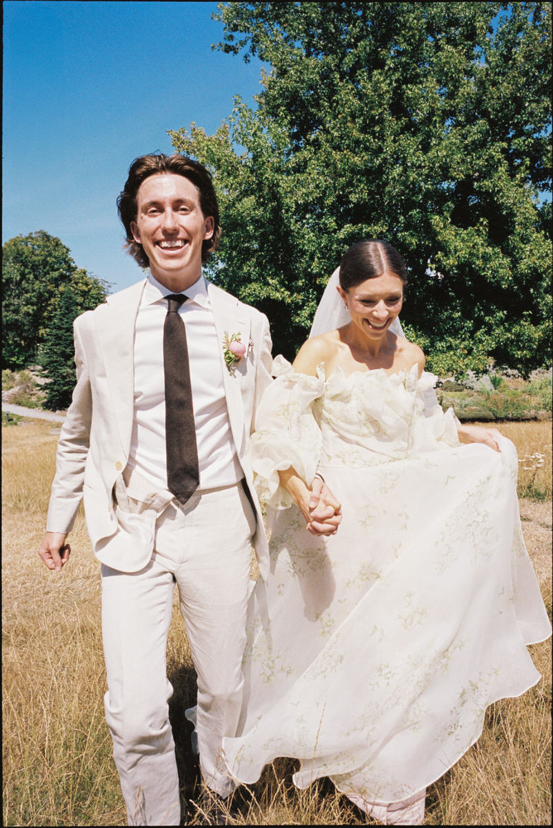 35mm film photo of smiling wedding couple walking through a grass field at UBC Botanical Garden