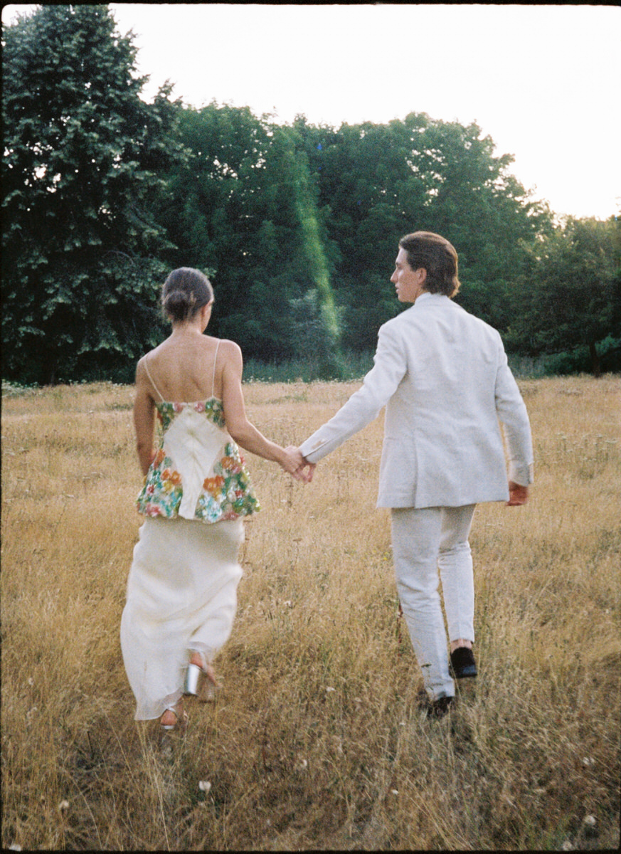 35mm film photo of bride in Markarian and groom in Suit Supply walking in a golden grass field at UBC Botanical Garden