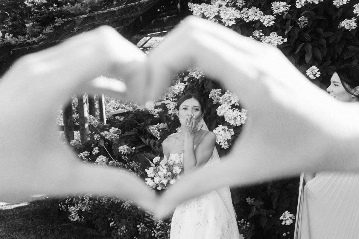 fun cinematic photo of bride blowing a kiss at the camera while a guest frames her with a heart using her hands