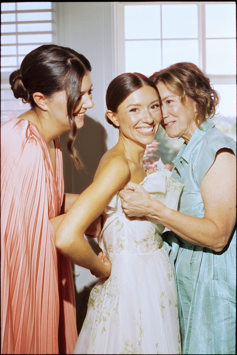 35mm film photo of bride helped into her Monique Lhuillier gown by her sister and mother