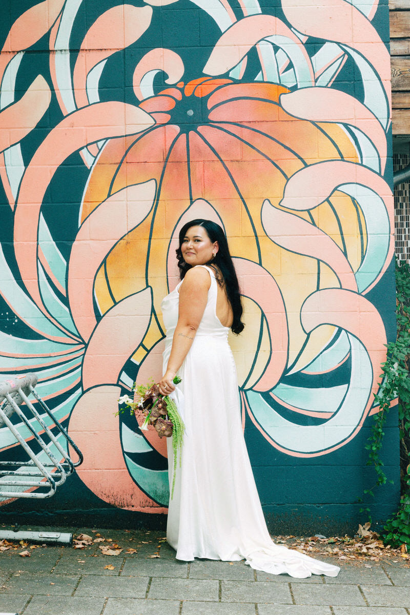wasian bride holding a bouquet while standing in front of a mural in vancouver featuring a peach chrysanthemum flower
