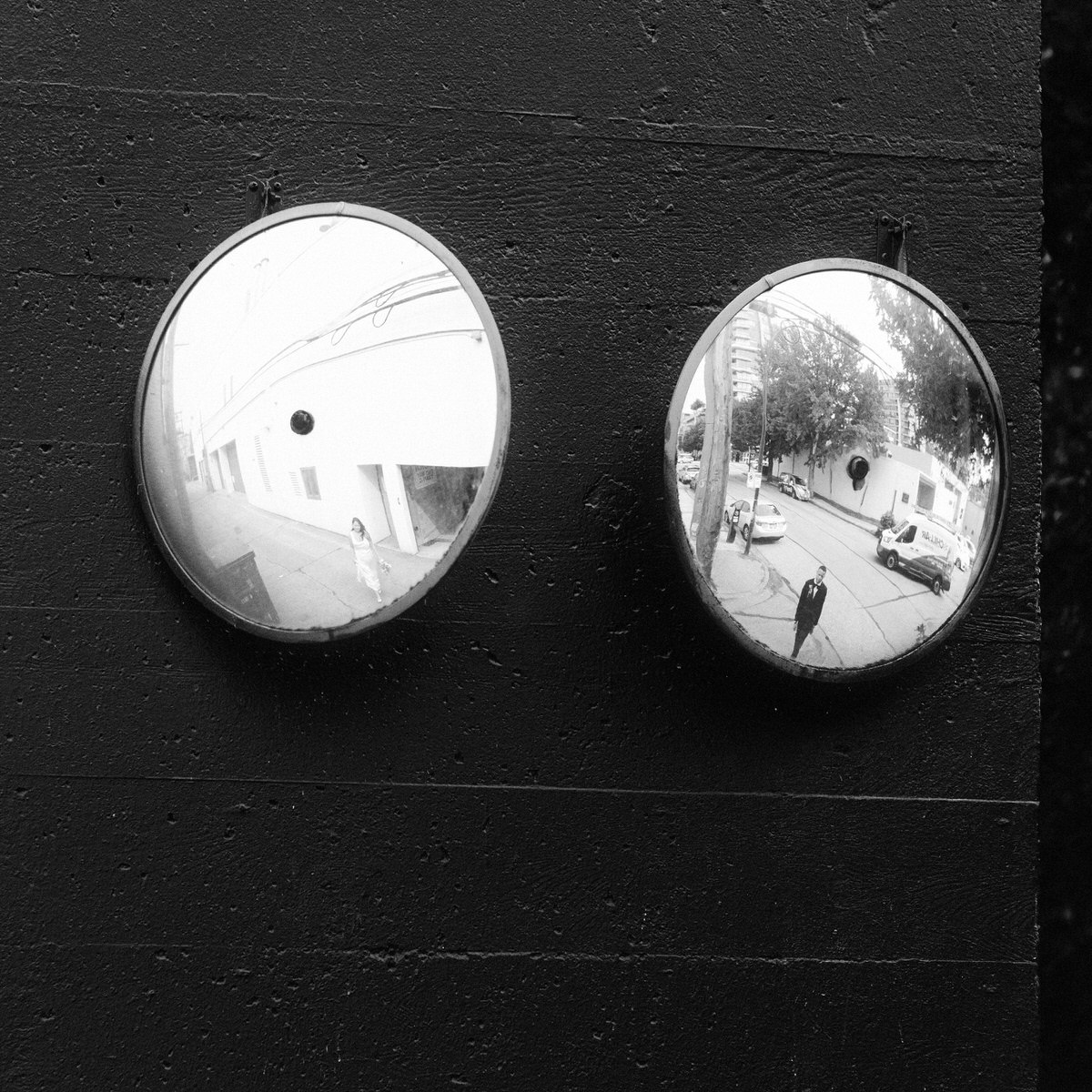 a wedding couple posing on the street while being reflected in two convex security mirrors