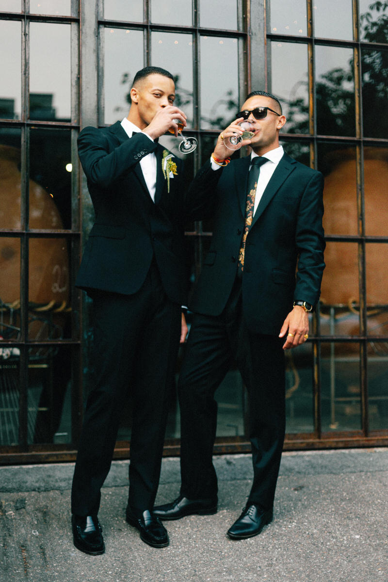 stylish groom in emporio armani drinking wine alongside an equally stylish wedding guest outside la fabrique st george winery in vancouver