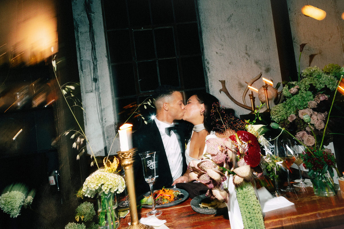 couple kissing during a wedding reception at la fabrique st george. they are surrounded by contemporary florals and candlelight